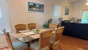 A dining area with a glass-top table surrounded by wicker chairs, a green table runner, and a bowl of fruit. -  Casa Capri Beautiful Tropical with 3 King Suites - 2 miles to beach (Key West)