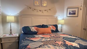 Een slaapkamer met een bed, twee nachtkastjes, een hoofdbord, wanddecoratie en een deur.