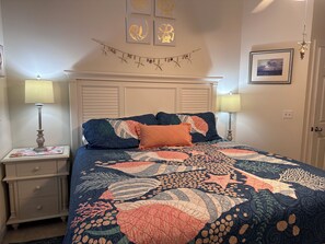 Une chambre à coucher comprenant un lit, deux tables de chevet, une commode, une tête de lit, des œuvres d’art murales et une porte.