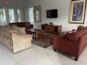 Un salon avec un canapé beige, un canapé rouge, une table basse en bois et un téléviseur fixé au mur.