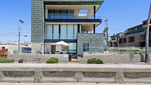 A modern two-story building with large windows, a balcony, and a small outdoor seating area with an umbrella. - Indoor/Outdoor living on the ocean front. (San Diego)