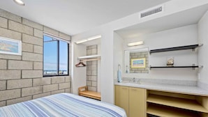 A bedroom with a bed, a window, a bathroom with a sink and mirror, and a view of the beach. - Indoor/Outdoor living on the ocean front. (San Diego)