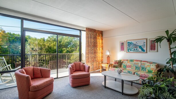 A modern living room with a large sliding glass door leading to a balcony, a sofa, two armchairs, a coffee table, and a lamp.