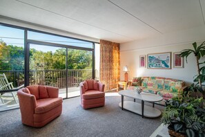 Un salon moderne doté d’une grande porte-fenêtre coulissante donnant sur un balcon, d’un canapé, de deux fauteuils, d’une table basse et d’une lampe.