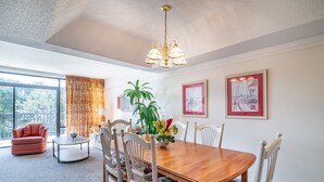 A dining area with a wooden table, floral chairs, a red sofa, a small side table, and a potted plant.