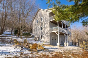 A two-story building with a balcony, wooden chairs, and a snow-covered yard.