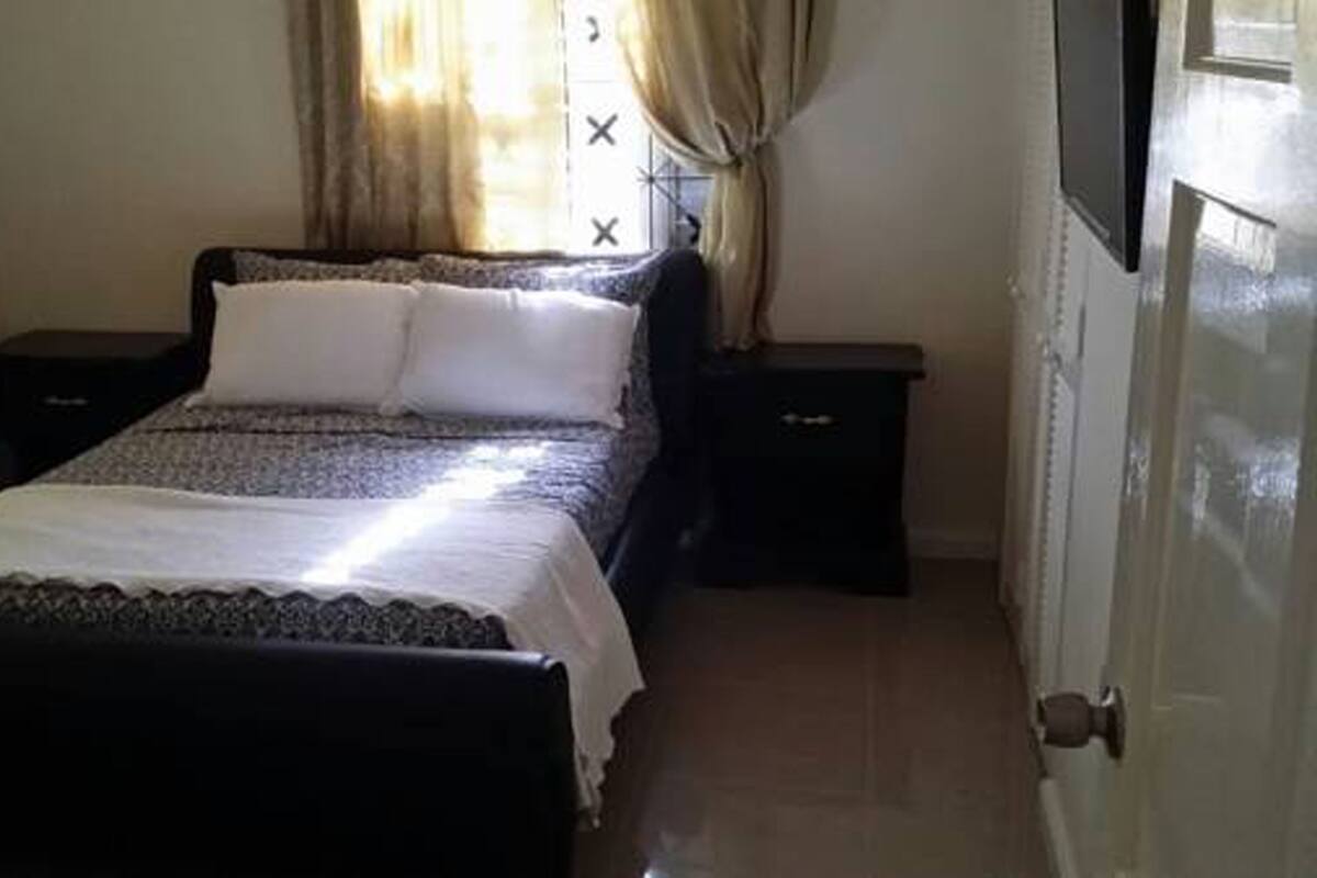 A small, neatly arranged bedroom with a bed, two bedside tables, and a window with curtains.