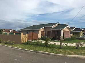 A single-story house with a green roof, a front porch, and a gated driveway.