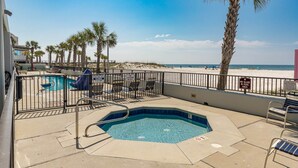 A pool area with a hot tub, lounge chairs, and a view of the beach.