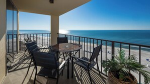 A balcony with a round table and chairs, overlooking a beach with the ocean in the background.