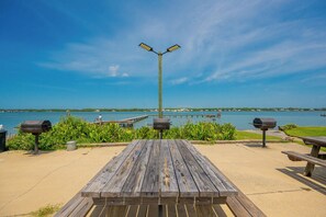 A picnic area with a wooden table and benches, a trash can, and a street lamp.