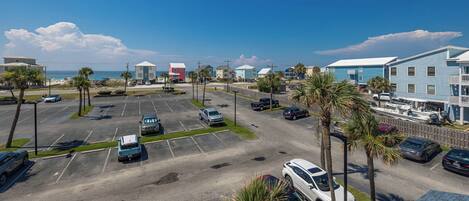 A parking lot with several cars, palm trees, and buildings with a beach view.