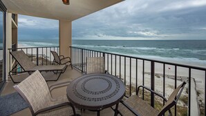 A balcony with a round table and chairs, overlooking a beach with a railing and a flag. - 1 BR 1 BA ~ Phoenix I ~ Condo 1074 (Orange Beach)