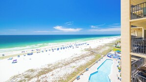 A beach view from a hotel balcony with a pool and beach umbrellas.