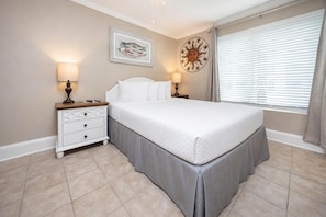 A bedroom with a bed, nightstands, a wall clock, and a window with blinds.