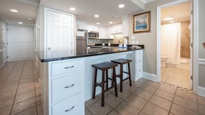 A modern kitchen with white cabinetry, a black countertop, and two bar stools.