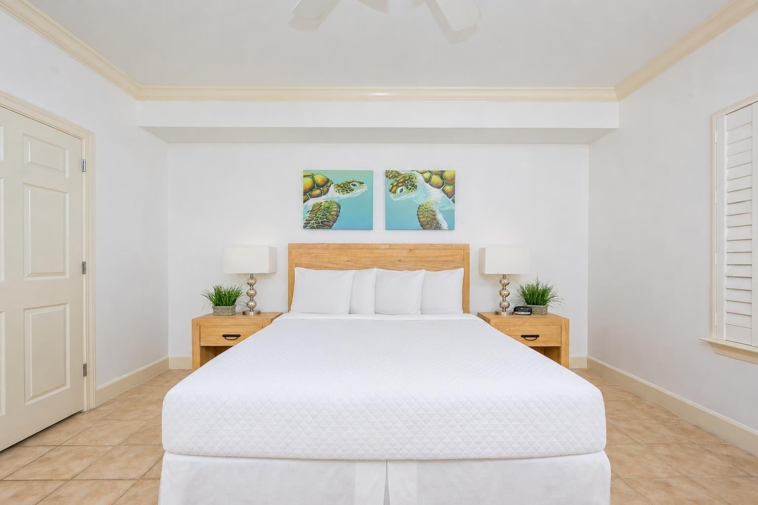A hotel room with a large bed, two nightstands with lamps, a door, and two wall art pieces.
