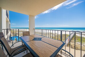 Un balcon avec une table et des chaises, donnant sur une plage et l’océan.