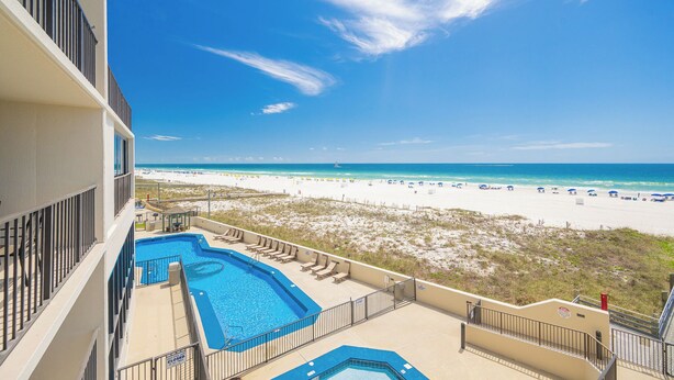 A pool area with lounge chairs, a view of the beach, and a clear sky. - RELAX on the BEACH! **Gulf Front 2 Bedroom at Phoenix III (Orange Beach)