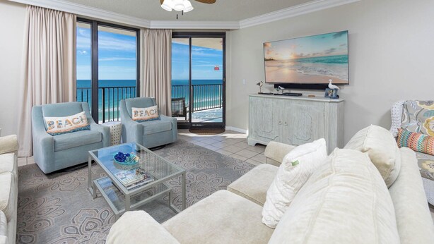 A spacious living room with a large window offering a view of the ocean, a ceiling fan, and a flat-screen TV on a cabinet.