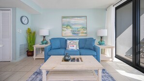 Un salon avec un canapé bleu, deux tables d’appoint avec des lampes, une table basse, un tableau et une horloge au mur.