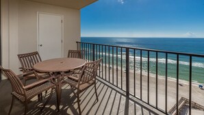 A balcony with a table and chairs, overlooking a beach with the ocean and a clear sky. - **WEEKLY SPECIALS!** Phoenix II - 11th Floor - 2 Bedroom (Orange Beach)