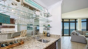 A kitchen with a granite countertop, a built-in sink, and a glass display shelf above the counter. - The Oasis, Unit 2209 — Luxury 3BR/4BA Gulf-Front Condo with Resort Amenities (Orange Beach)