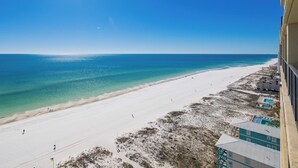 Blick auf einen Strand mit blauem Himmel, sandigem Ufer und Gebäuden entlang der Küste.