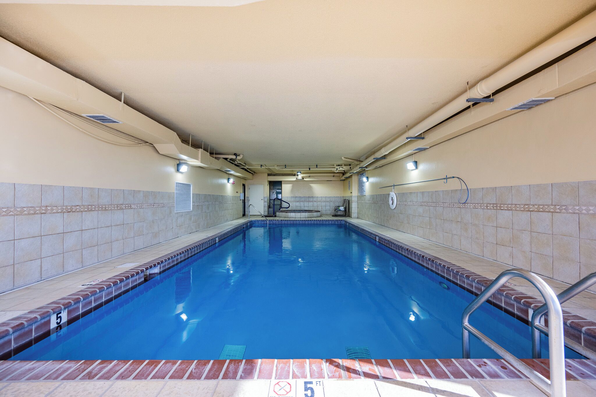 A rectangular indoor swimming pool with a tiled border, a visible depth marker, and a pool ladder.
