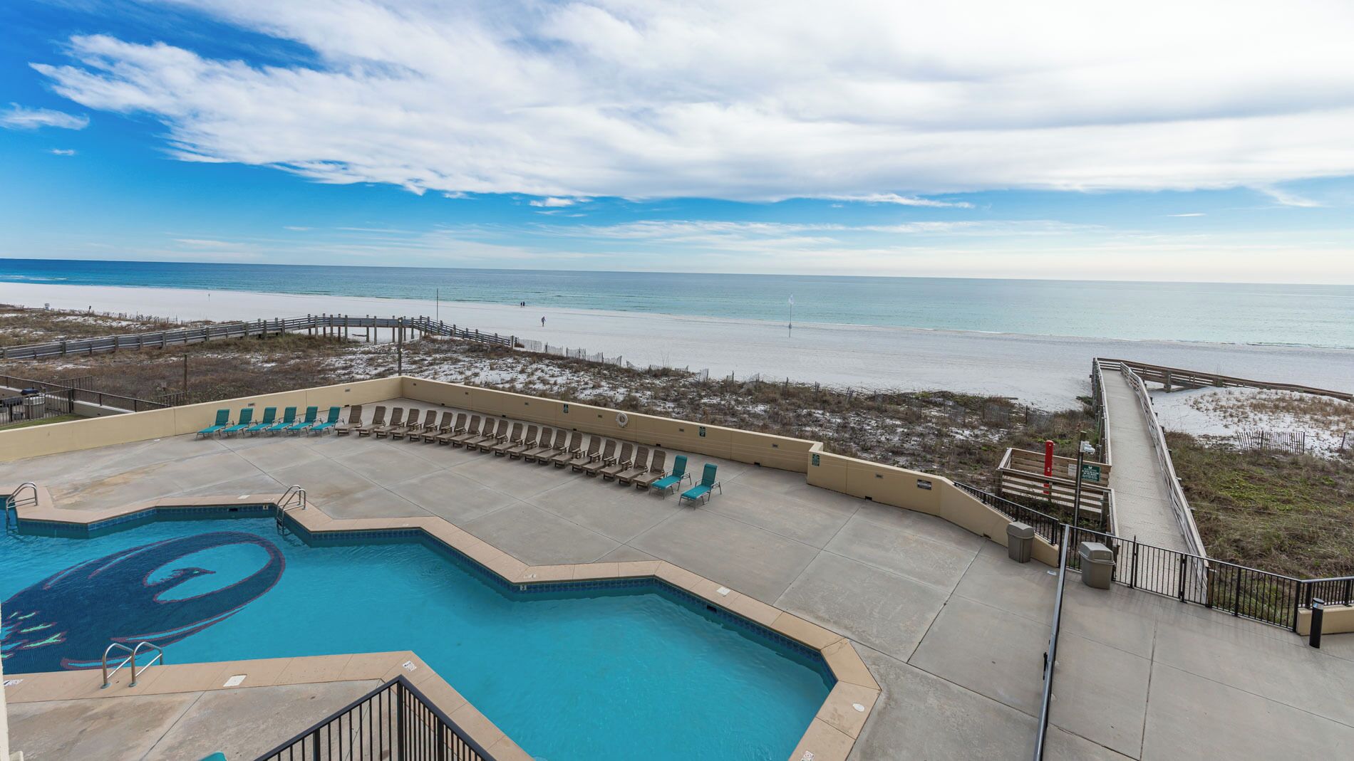 A pool area with lounge chairs and a view of the beach.