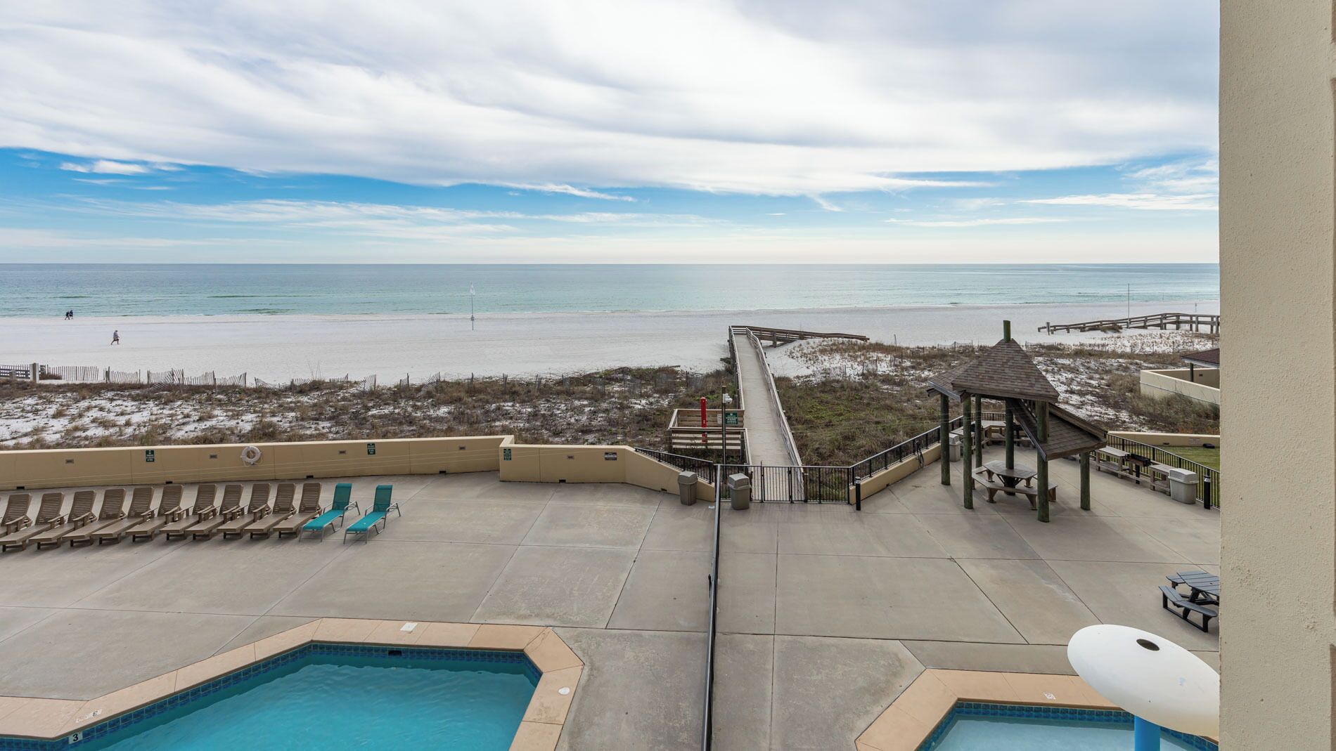 A pool area with a view of the beach, including lounge chairs and a gazebo.