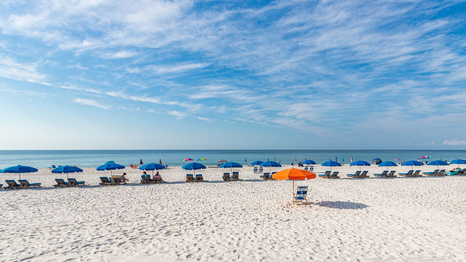 Een strand met rijen ligbedden en parasols, een heldere lucht en de oceaan op de achtergrond.