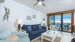 A living room with a sofa, armchair, and coffee table, a balcony with outdoor seating, and decorative wall art.