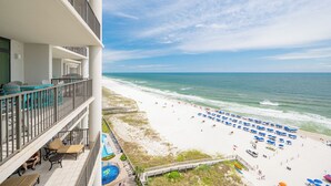 A hotel balcony with outdoor seating and a pool, overlooking a beach with umbrellas and a clear view of the ocean. - The Oasis of Orange Beach 1104 (Orange Beach)