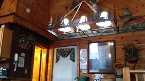 A rustic wooden interior with a wooden bench, a hanging light fixture, and a window with a curtain. - ARCADE GAMES💥Recent Peacock Sightings💥May weekdays up till the 21th $75 to $85 (Pigeon Forge)
