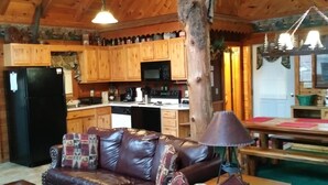 A rustic cabin interior with a leather sofa, wooden ceiling beams, a dining table, and a kitchen area. - ARCADE GAMES💥Recent Peacock Sightings💥May weekdays up till the 21th $75 to $85 (Pigeon Forge)