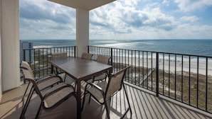 Un balcon avec une table et des chaises, donnant sur une plage et l’océan.