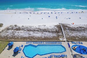 A beach with a swimming pool, sun loungers, and umbrellas.