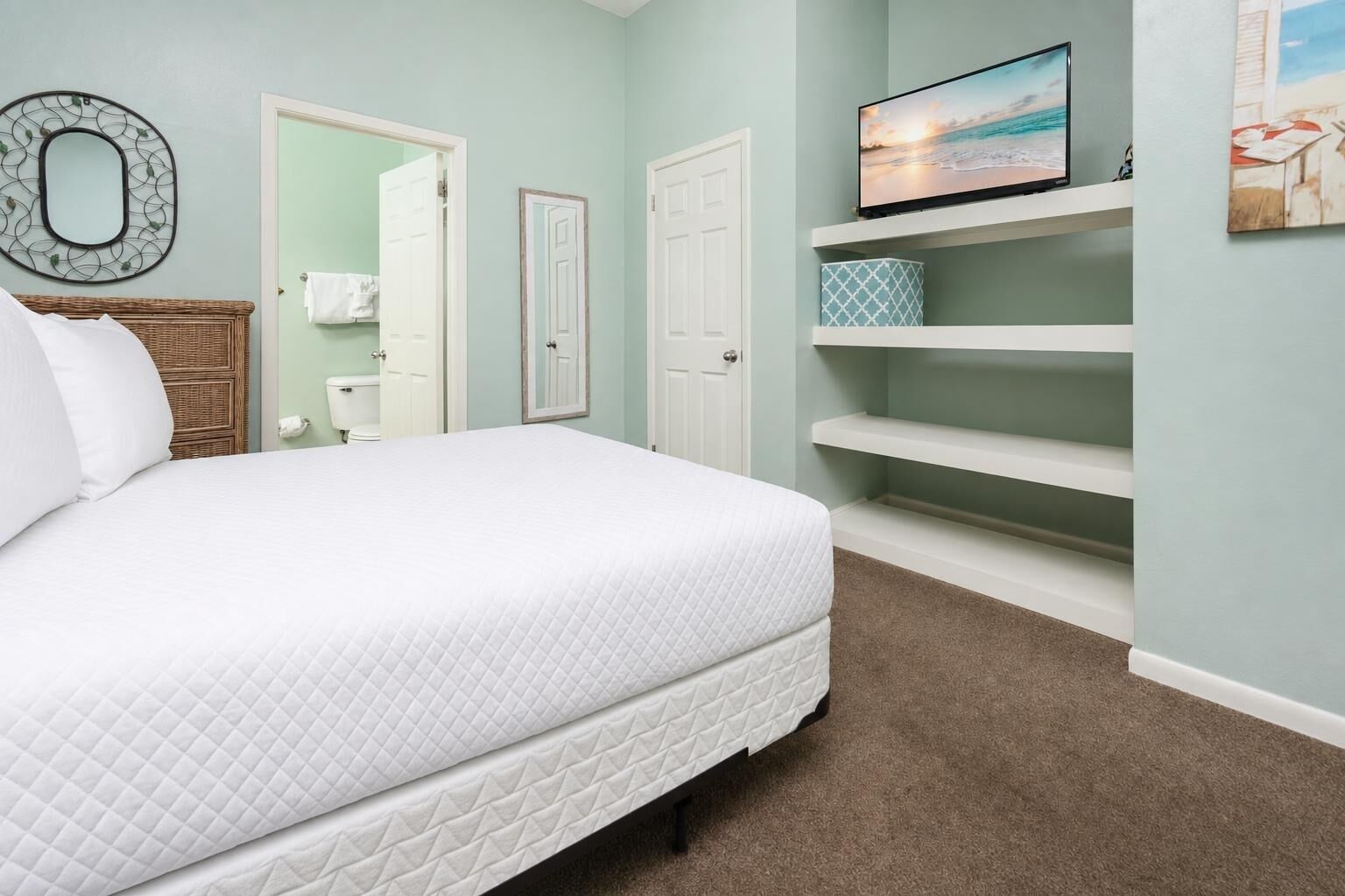 Un dormitorio con cama, televisor en un estante y baño con inodoro y perchero para toallas.