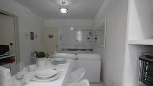 Una habitación estrecha con paredes blancas, una mesa de comedor para dos, una pequeña kitchenette y un horno empotrado.