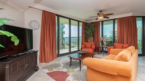 A living room with a TV, orange sofa, and a large window with curtains. - *Guest's Choice* 2 Bedroom @ Phoenix On The Bay!* (Orange Beach)