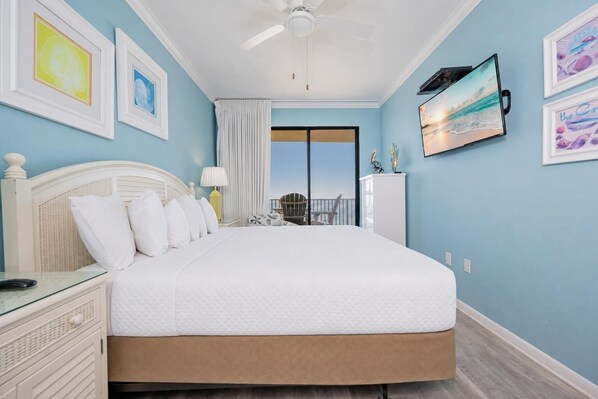 A hotel room with a large bed, a ceiling fan, a TV, and a balcony with a view.