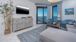 A modern living room with a television, a sofa, a coffee table, and a balcony with a view.