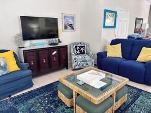 Una sala de estar con televisor, un sofá azul, una mesa de centro de mimbre y un tapete estampado.