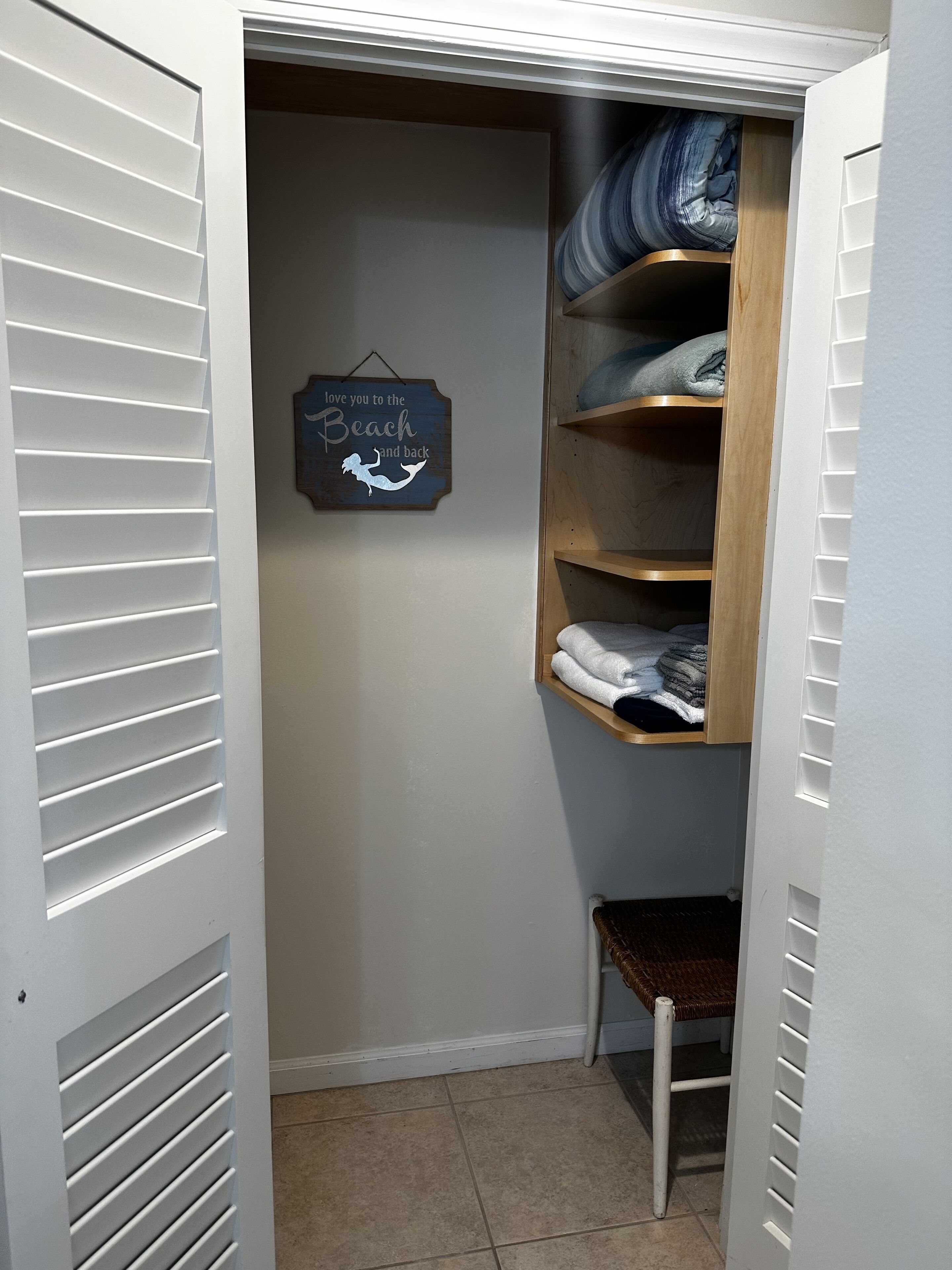 A closet with white sliding doors, a wooden shelf unit, and a wall-mounted sign that reads "love you to the Beach and back".