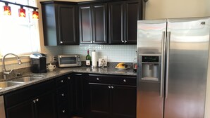 A kitchen with dark cabinets, a stainless steel refrigerator, a microwave, and a coffee maker. - Haywood House: West Asheville's Newly Restored And Most Walkable Rental! (Asheville)
