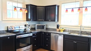 A modern kitchen with dark cabinets, stainless steel appliances, and a granite countertop. - Haywood House: West Asheville's Newly Restored And Most Walkable Rental! (Asheville)