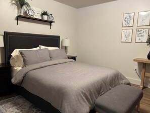 Un letto rifatto con cura, un comodino con una lampada e un piccolo ripiano con oggetti decorativi.