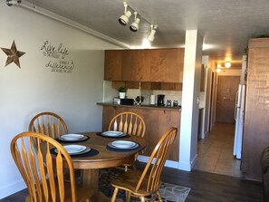 Un comedor con una mesa y sillas de madera, una cocina al fondo y un pasillo que conduce a una puerta.