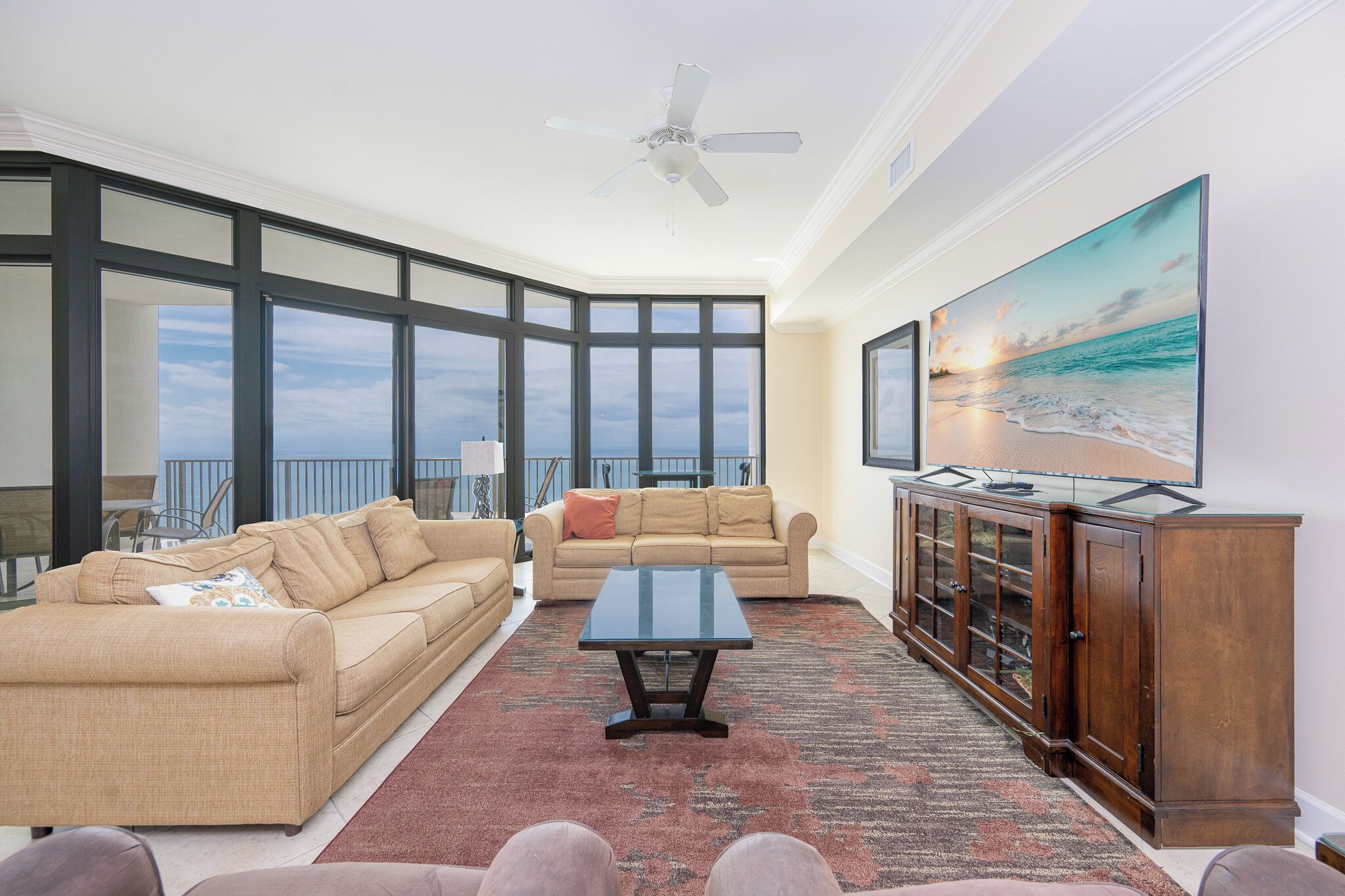 A spacious living room with a large window, a ceiling fan, a beige sofa, a coffee table, and a wooden cabinet.